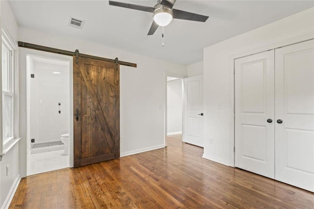 unfurnished bedroom featuring connected bathroom, a barn door, dark hardwood / wood-style floors, and ceiling fan