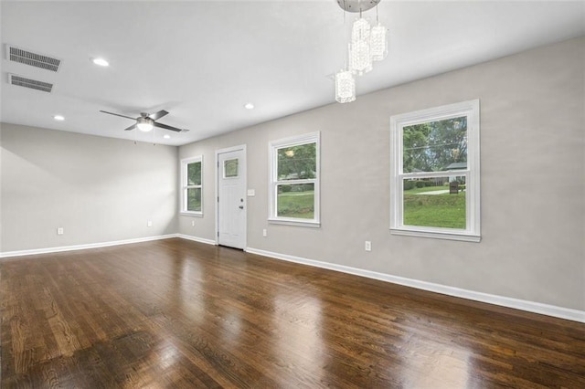 spare room featuring a wealth of natural light, ceiling fan with notable chandelier, and dark hardwood / wood-style flooring