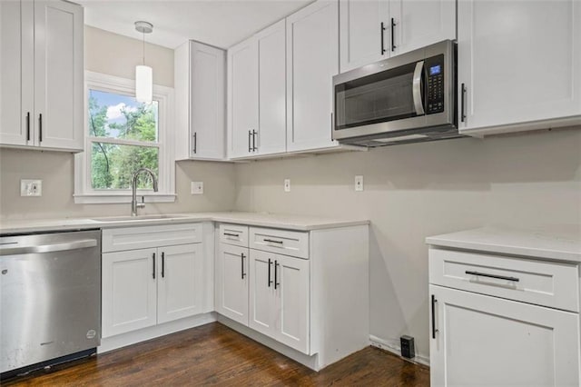 kitchen with sink, dark hardwood / wood-style flooring, hanging light fixtures, stainless steel appliances, and white cabinets