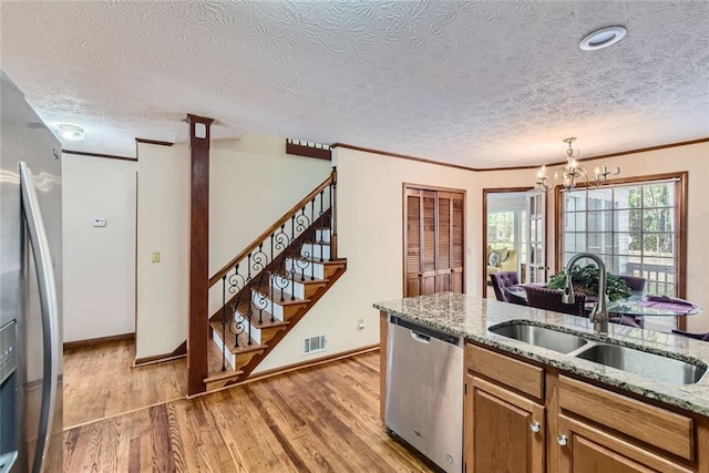 kitchen with brown cabinetry, visible vents, light wood-style flooring, a sink, and stainless steel appliances