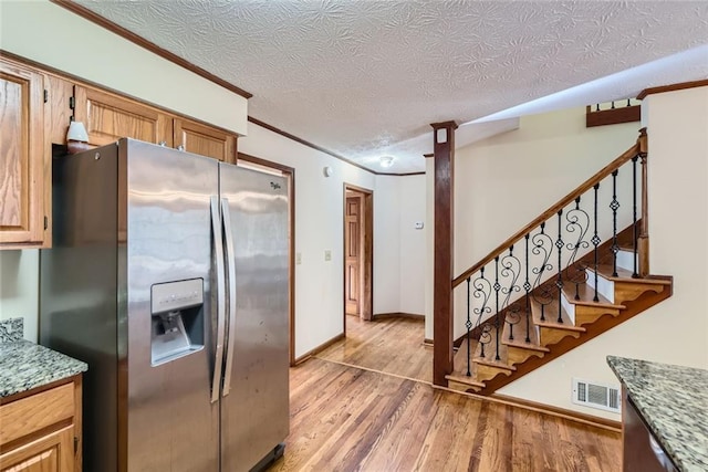 kitchen featuring visible vents, light wood-style flooring, stainless steel refrigerator with ice dispenser, ornamental molding, and a textured ceiling