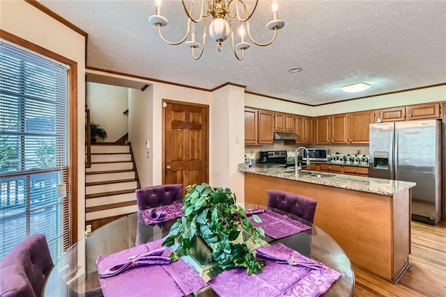 kitchen featuring under cabinet range hood, light wood-style flooring, appliances with stainless steel finishes, brown cabinetry, and a notable chandelier