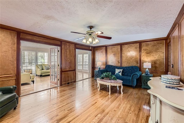 living area with light wood finished floors, a decorative wall, french doors, and crown molding