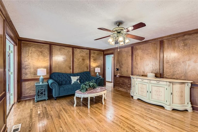 living area with a textured ceiling, light wood-style flooring, visible vents, and ornamental molding