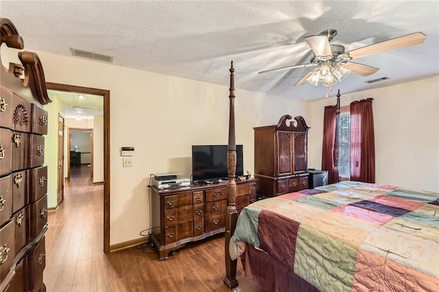 bedroom with visible vents, a textured ceiling, attic access, and wood finished floors