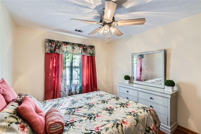 bedroom featuring baseboards, a ceiling fan, visible vents, and a textured ceiling