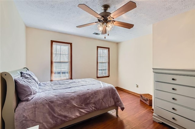 bedroom with a ceiling fan, baseboards, wood finished floors, visible vents, and a textured ceiling