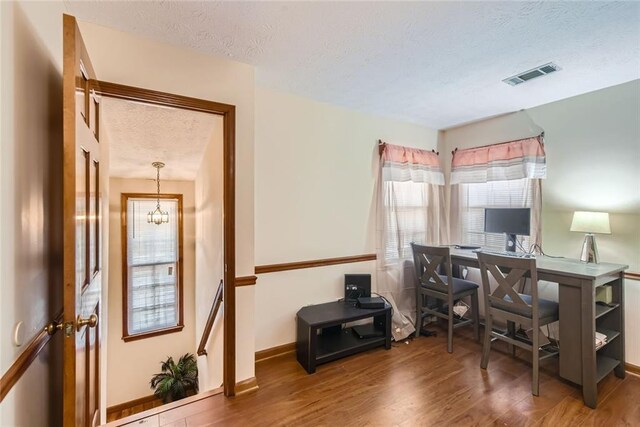 office area featuring wood finished floors, baseboards, visible vents, a textured ceiling, and a chandelier