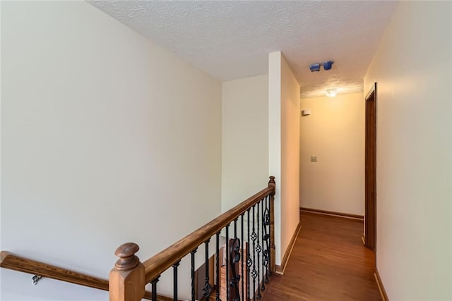 hallway with wood finished floors, an upstairs landing, baseboards, and a textured ceiling