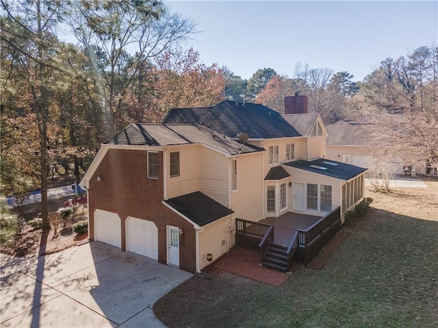 rear view of house with a chimney, brick siding, an attached garage, and driveway