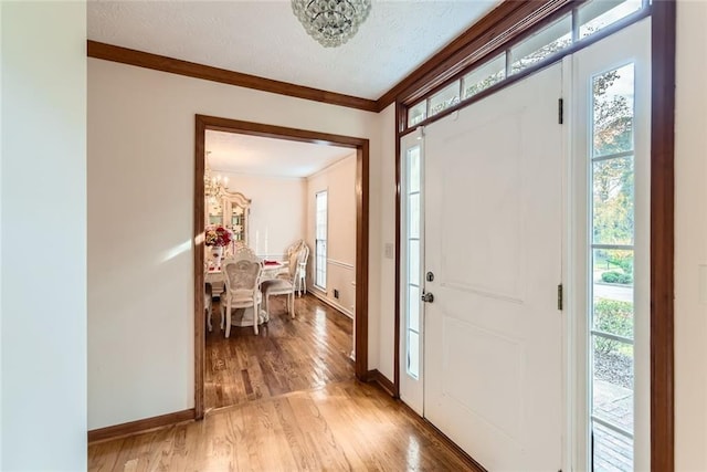 entrance foyer featuring a wealth of natural light, light wood-type flooring, a textured ceiling, and ornamental molding