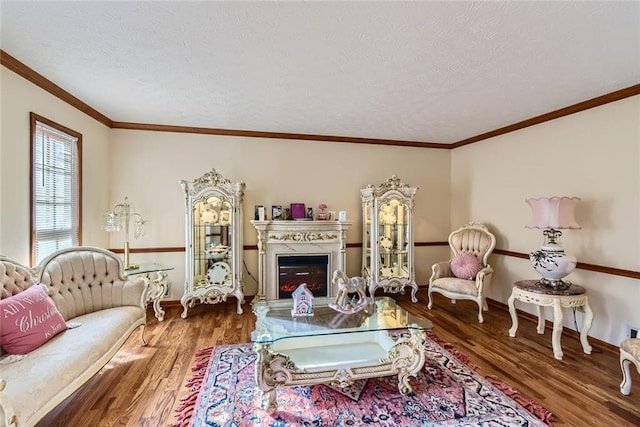 living room with wood finished floors, baseboards, ornamental molding, a textured ceiling, and a glass covered fireplace