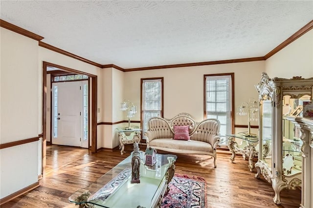 living room with a textured ceiling, crown molding, baseboards, and wood finished floors