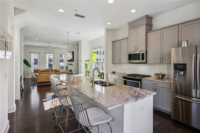 2034 Rockledge Rd NE, Atlanta, GA 30324 - kitchen with stainless steel appliances, gray cabinetry, a sink, light stone countertops, and a center island with sink