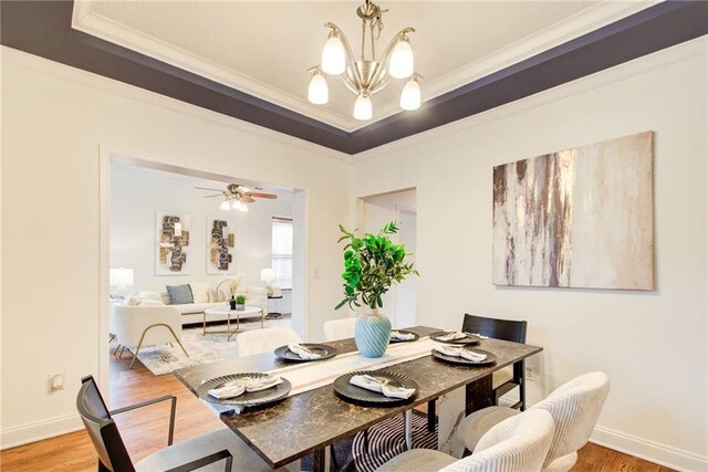 dining space with hardwood / wood-style flooring, ceiling fan with notable chandelier, ornamental molding, and a tray ceiling