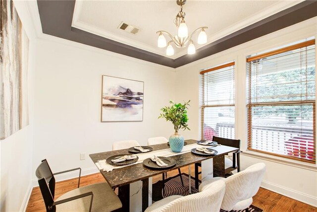 dining area featuring hardwood / wood-style flooring, a notable chandelier, a raised ceiling, and crown molding