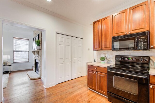 kitchen with backsplash, black appliances, light wood-type flooring, ornamental molding, and a fireplace