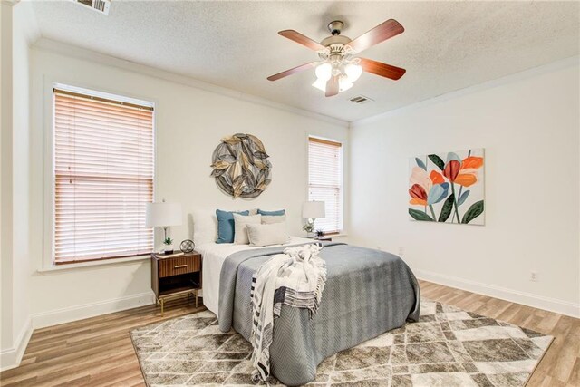 bedroom with hardwood / wood-style flooring, ceiling fan, ornamental molding, and a textured ceiling