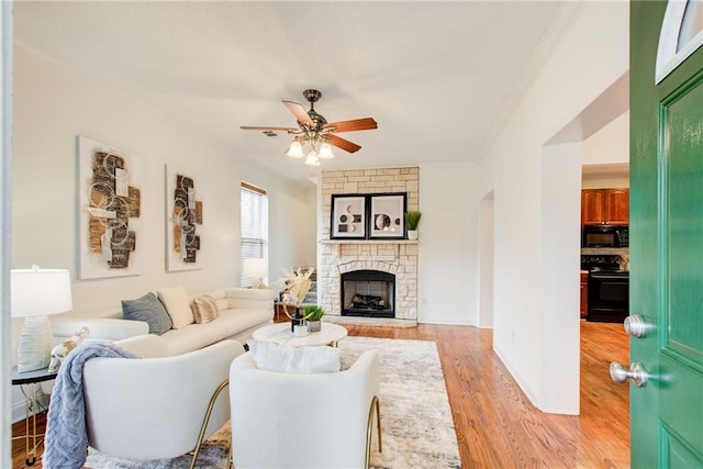 living room featuring light wood-type flooring, a stone fireplace, ceiling fan, and ornamental molding