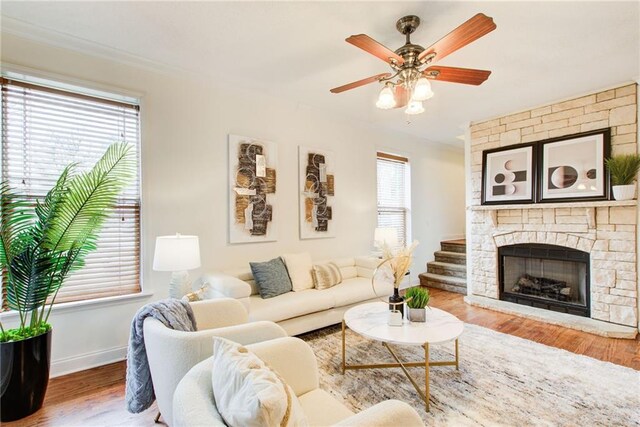 living room with wood-type flooring, a stone fireplace, and ceiling fan