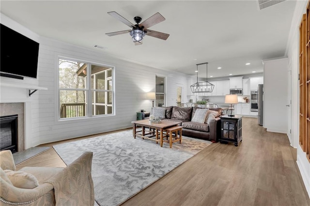 living room featuring a premium fireplace, light wood finished floors, ceiling fan, and visible vents