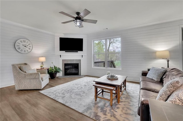 living room with crown molding, wood finished floors, a ceiling fan, and a glass covered fireplace