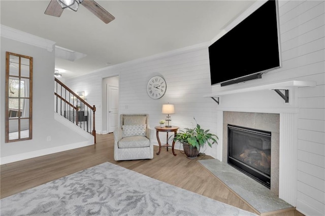 sitting room with crown molding, ceiling fan, a fireplace, wood finished floors, and stairs