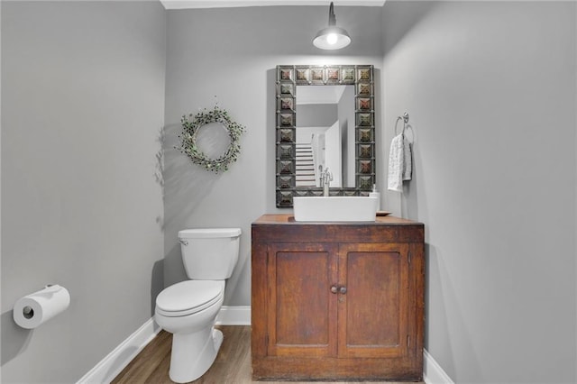 half bath with vanity, baseboards, toilet, and wood finished floors