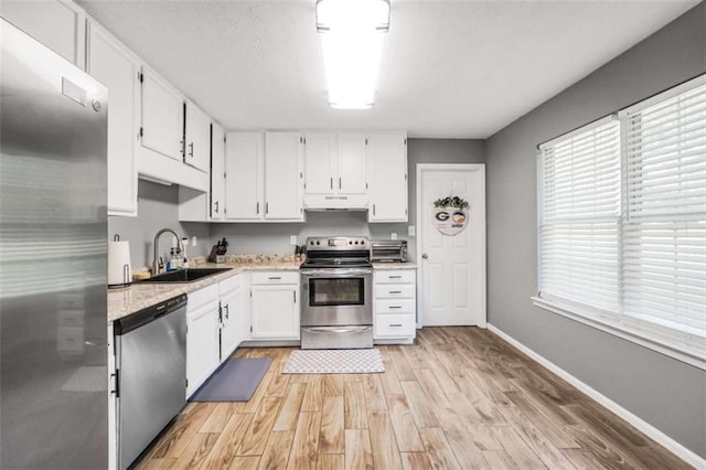 kitchen with appliances with stainless steel finishes, white cabinetry, a sink, light wood-type flooring, and under cabinet range hood