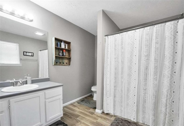 bathroom with a textured ceiling, toilet, wood finished floors, vanity, and baseboards