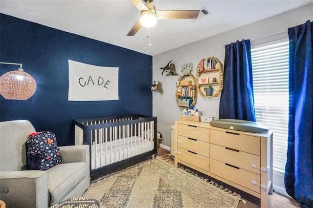 bedroom featuring an accent wall, a crib, a ceiling fan, and baseboards