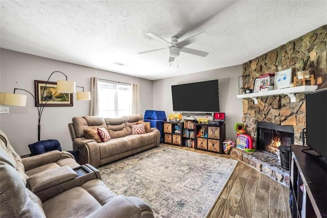 living room with a textured ceiling, a fireplace, wood finished floors, and a ceiling fan