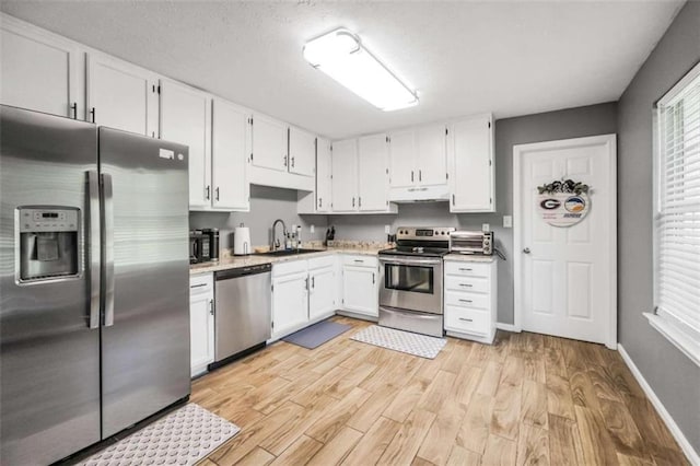 kitchen featuring under cabinet range hood, a sink, white cabinets, light countertops, and appliances with stainless steel finishes