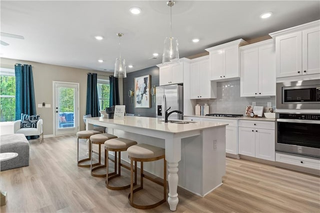 kitchen with pendant lighting, sink, stainless steel appliances, white cabinets, and a center island with sink