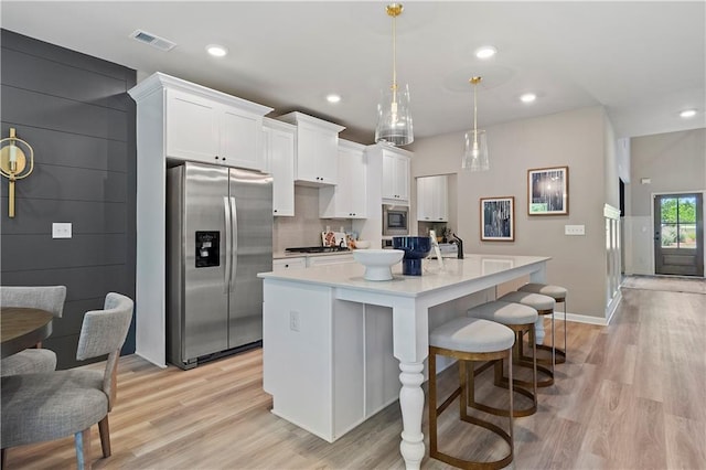 kitchen featuring white cabinetry, appliances with stainless steel finishes, a kitchen island with sink, and pendant lighting