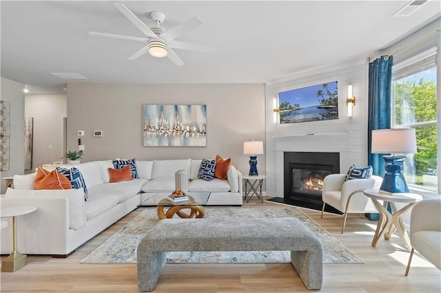 living room featuring ceiling fan, a large fireplace, and light wood-type flooring