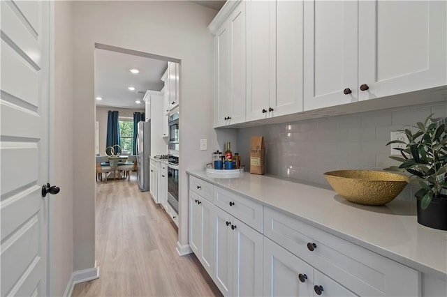 kitchen with backsplash, stainless steel appliances, light hardwood / wood-style floors, and white cabinets