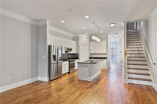 kitchen featuring a center island with sink, dark countertops, light wood-style flooring, stainless steel appliances, and a sink