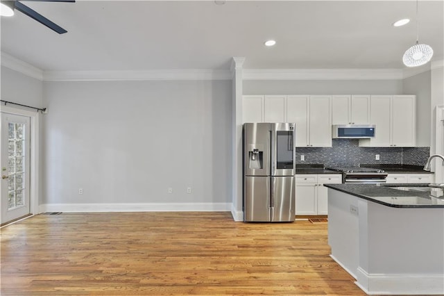 kitchen featuring light wood finished floors, stainless steel appliances, dark countertops, tasteful backsplash, and a sink