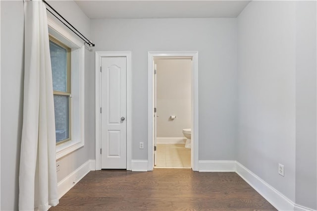 unfurnished bedroom with dark wood-style floors, baseboards, and connected bathroom