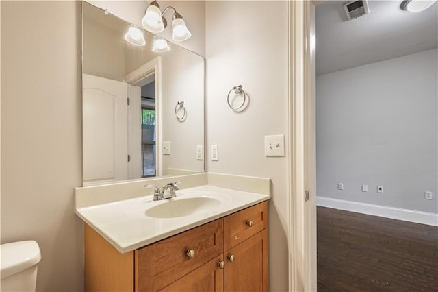 bathroom featuring visible vents, toilet, vanity, wood finished floors, and baseboards