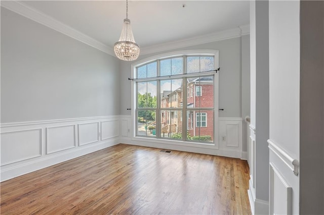 empty room with an inviting chandelier, visible vents, crown molding, and wood finished floors