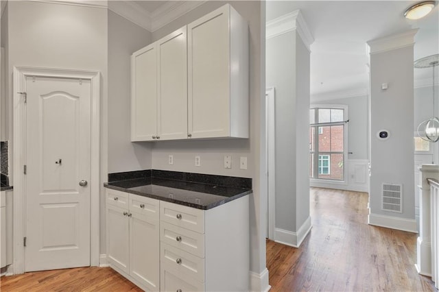 kitchen featuring white cabinetry, visible vents, light wood-style floors, ornamental molding, and dark stone countertops