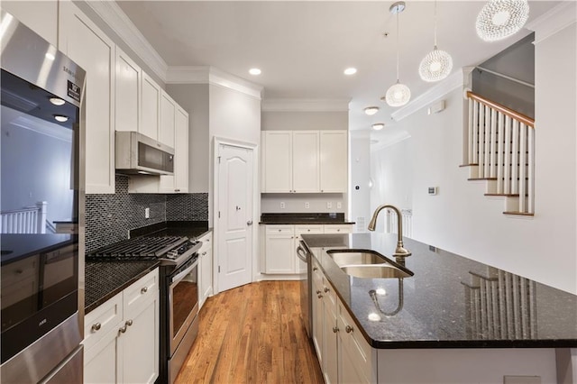 kitchen with light wood-style flooring, ornamental molding, a kitchen island with sink, stainless steel appliances, and a sink