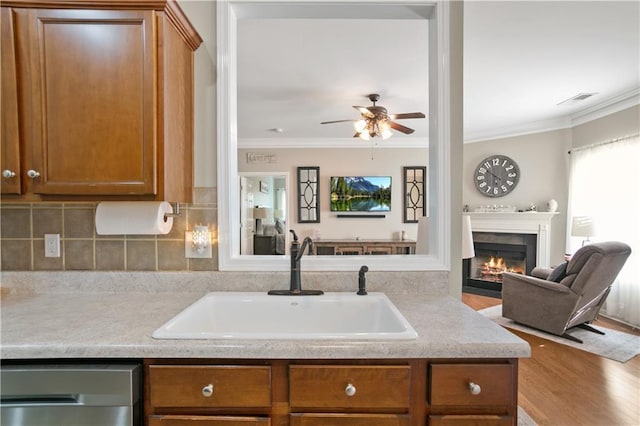kitchen featuring open floor plan, crown molding, a sink, dishwasher, and brown cabinetry