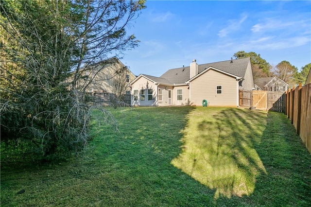 back of house with a fenced backyard, a chimney, and a yard