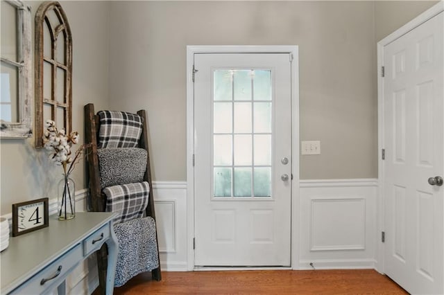 doorway to outside with wainscoting, wood finished floors, and a decorative wall