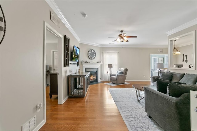 living area with crown molding, a ceiling fan, a fireplace with flush hearth, wood finished floors, and visible vents