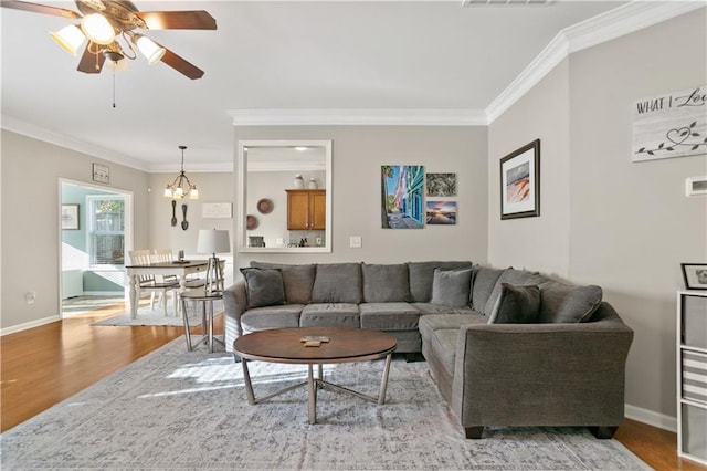 living area featuring ceiling fan with notable chandelier, crown molding, wood finished floors, and baseboards