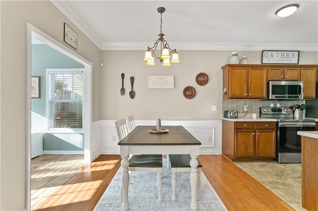 dining area with a chandelier, wainscoting, light wood-style flooring, a decorative wall, and ornamental molding